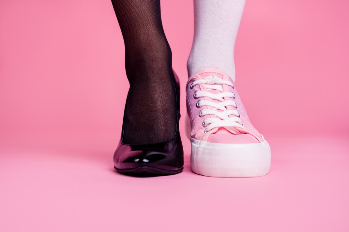 Nohy a obuv, dvě nohy, jedna v černých hedvábných punčochách s černými lodičkami a druhá v růžových punčochách a teniskách.
