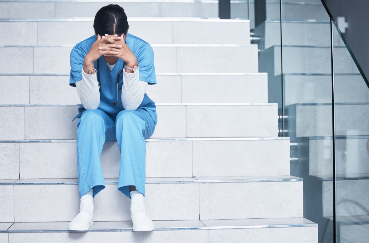 Zdravotní sestra sedí vyčerpaná na schodech a trpí syndromem vyhoření
