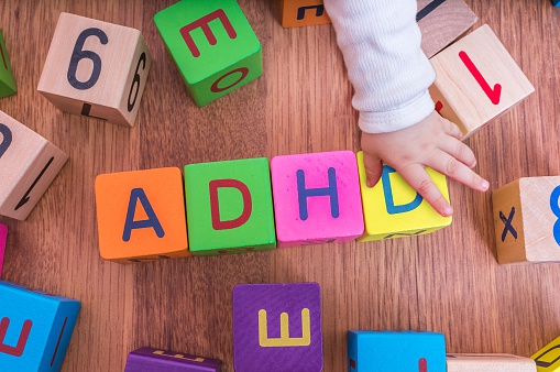 dětské kostičky s písmenky, poskládané tak, že vytvářejí název ADHD, u nich je dětská ruka