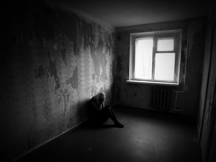 žena sedící v tmavé místnosti oprená o zed a rukama si drží tvár