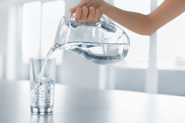 ruka nalévající čistou vodu z láhve do sklenice