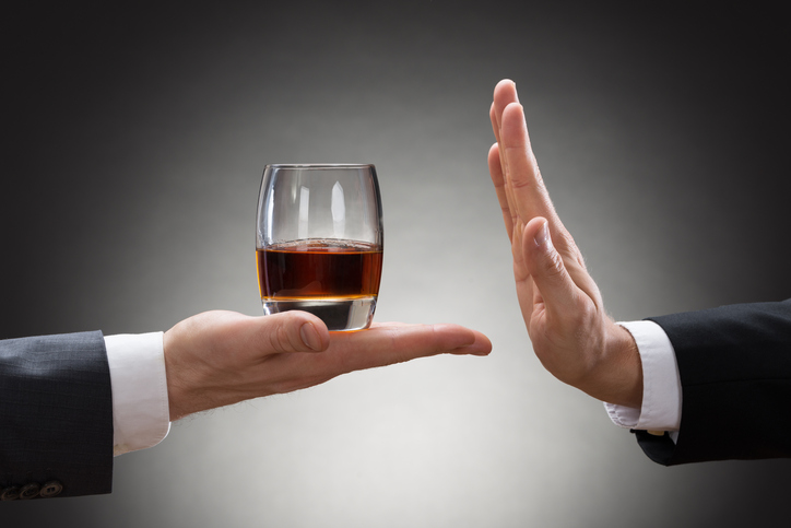 ruka člověka drží sklenici s alkoholem a druhá ruka jiného člověka ho odmítá