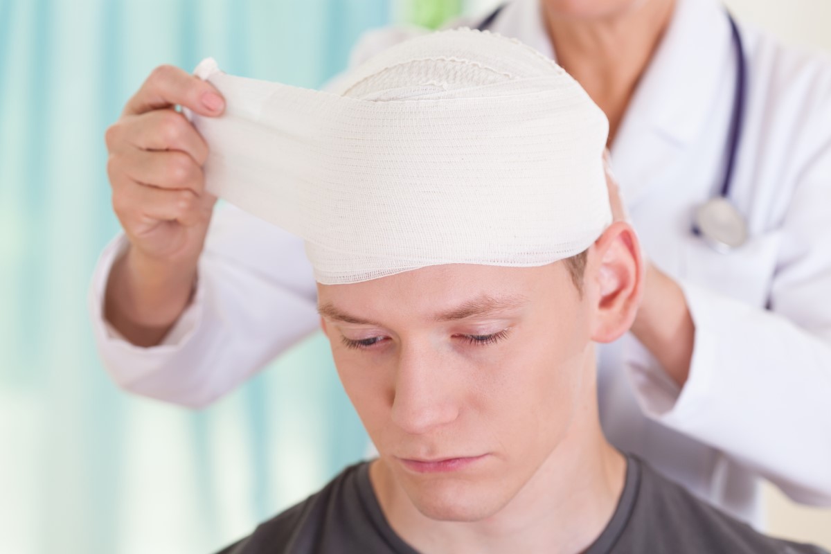 Bolest hlavy po nehodě, obvázaná hlava, lékař ošetřuje chlapce s poraněním hlavy