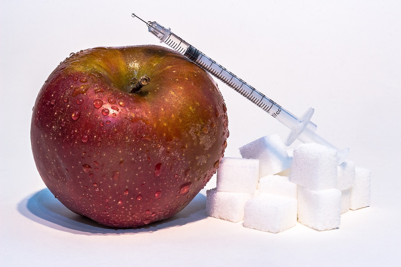 červené jablko, kostky cukru a inzulínová stříkačka