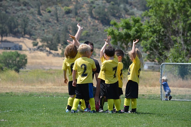 Deti ve žlutých dresech na fotbalovém hrišti. Teší se ve skupine spolu se svým trenérem.