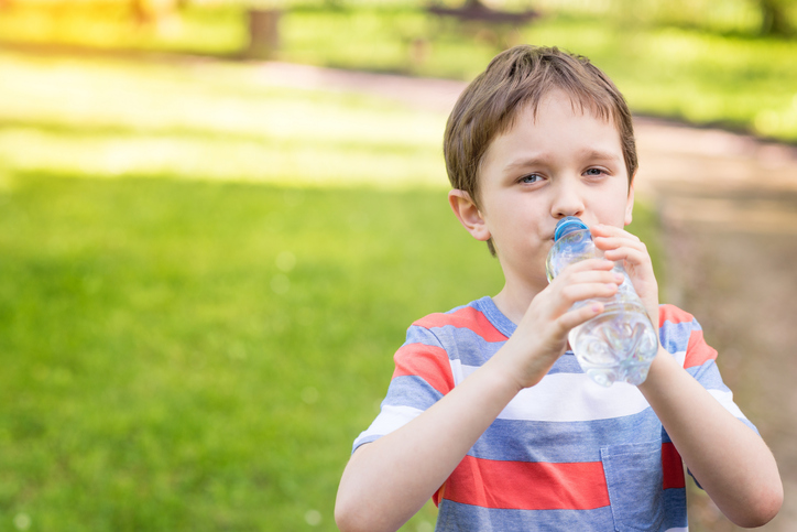 Chlapec pije vodu z láhve, zelená tráva na pozadí