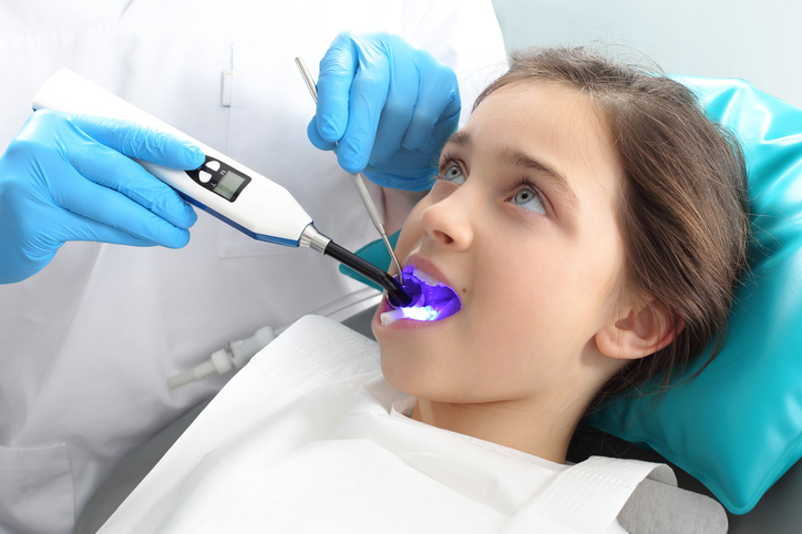 Dívka v zubařském křesle při ošetření zubařem