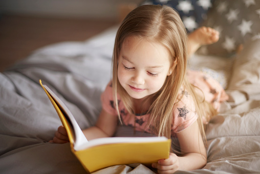 Děvčátko čte žlutou knihu na posteli