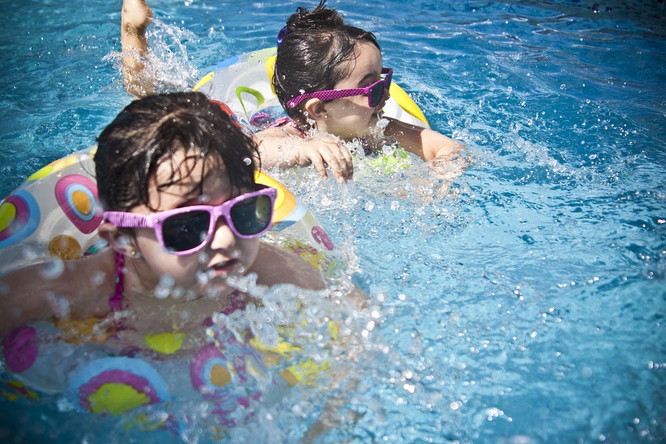 Dve deti se koupou ve vode. Mají slunecní brýle s ružovým rámem. Jsou v plovoucích kolech