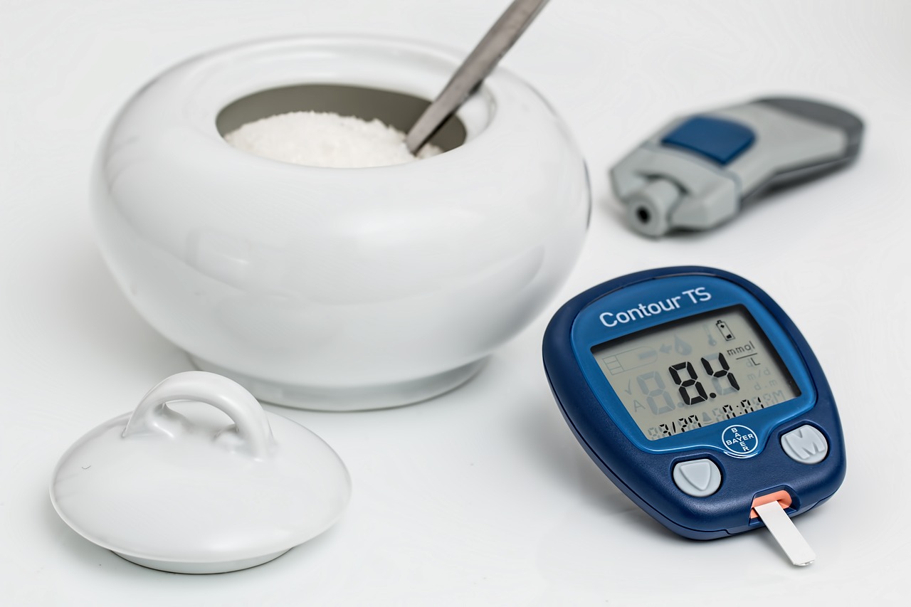 modrý glukometr na stole vedle nádoby s cukrem