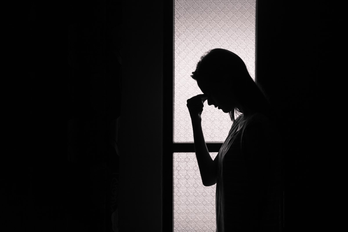 Migréna, citlivost na světlo, žena stojící v tmavé místnosti