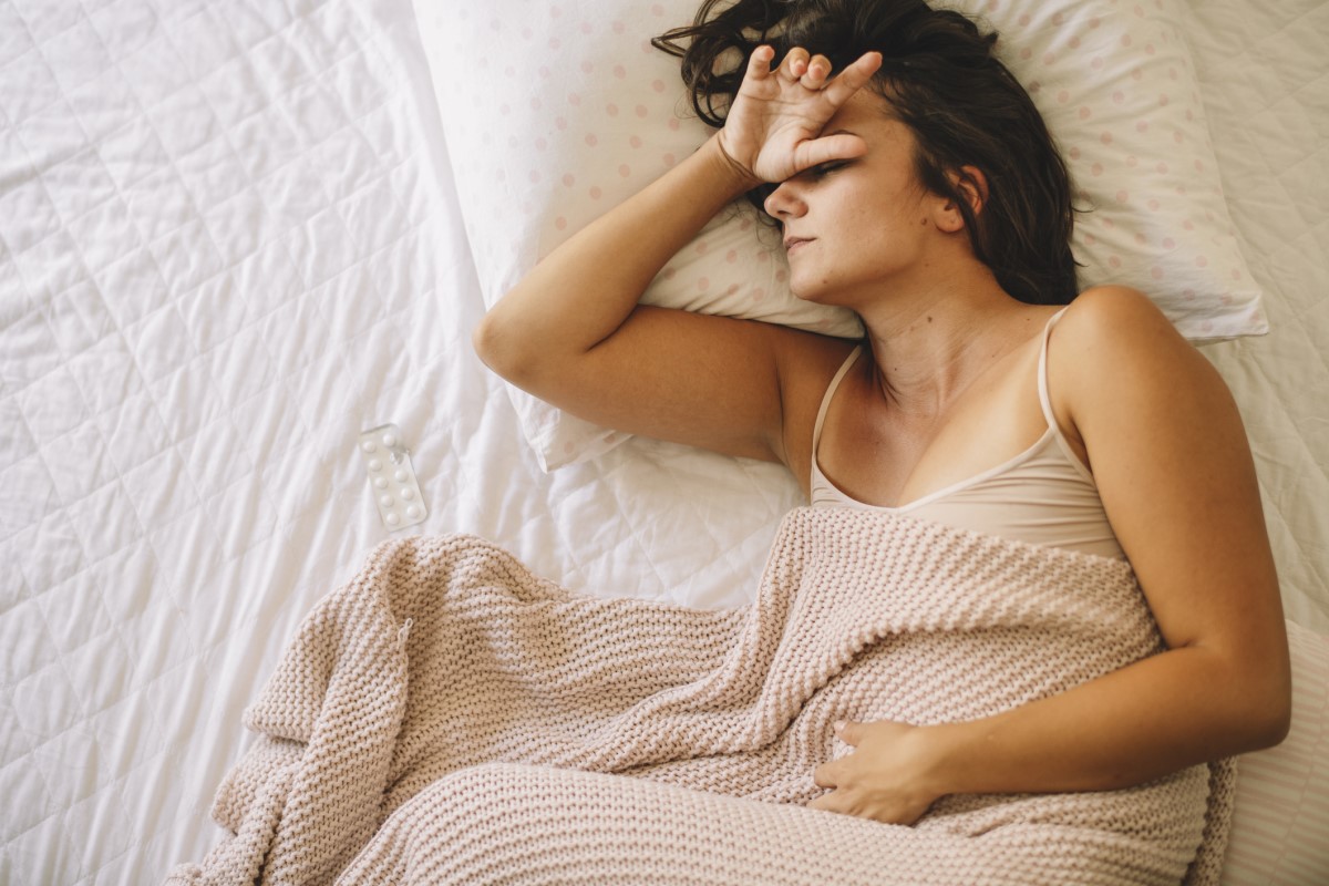 Žena trpí migrénou, leží v posteli a má zdravotní problémy.