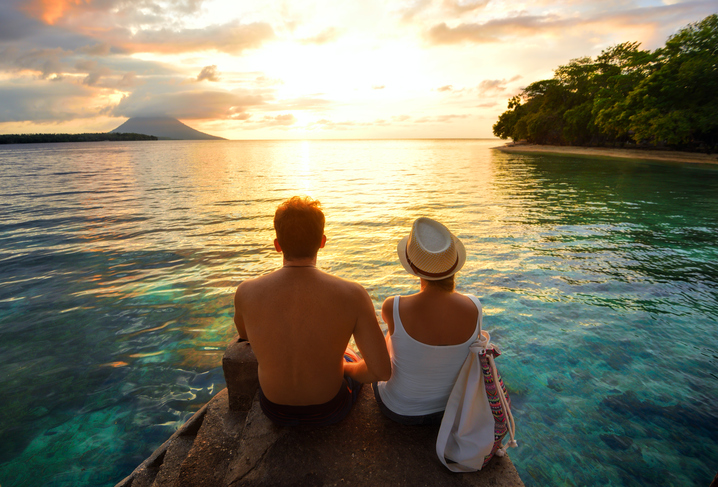 dvojice sedící na skále u moře při východu slunce