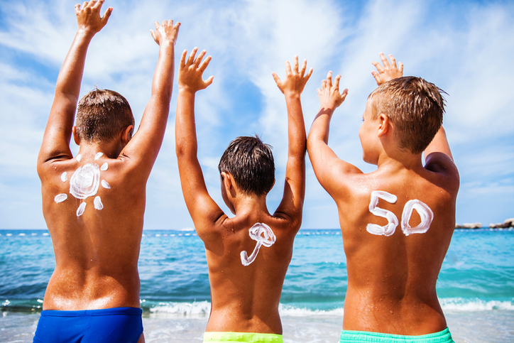 Opalovací krém pro děti s OF 50, děti jsou na pláži u moře a těší se, ruce mají nahoře