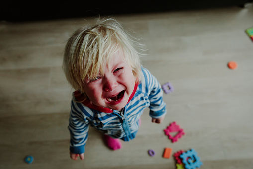 Plačící dítě, kolem jsou rozházené hračky