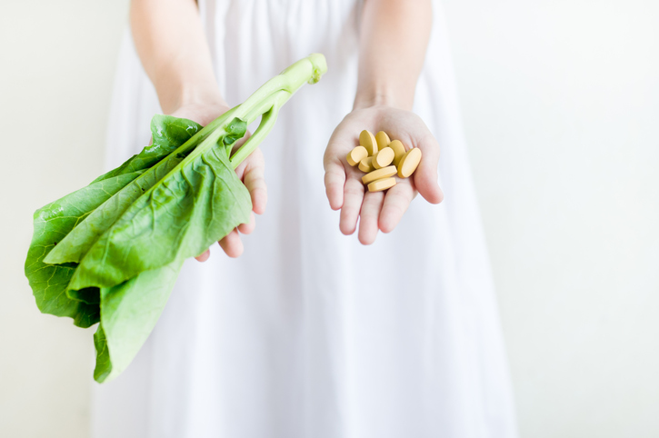 Ruce držící pilulky a listy salátu