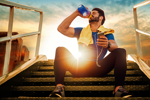 sportovec sedí na schodech. Západ slunce. Pije z dózy doplněk výživy.