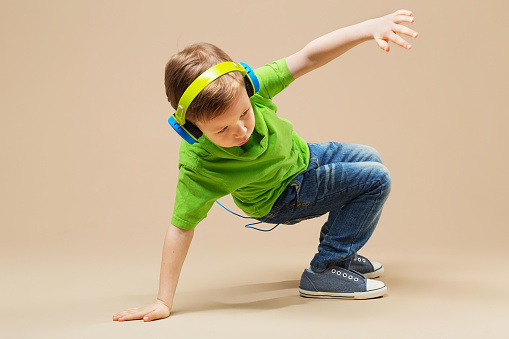 Dítě v zeleno tričku se sluchátky na ušák dělá break dance