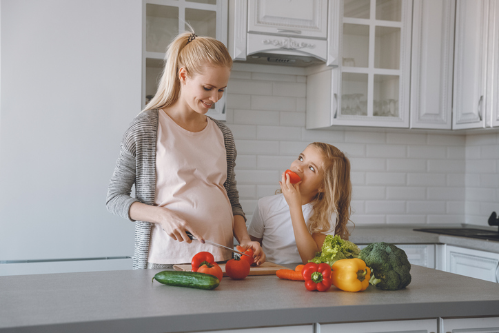 Tehotná matka s dcerou pripravují zdravé jídlo v kuchyni.