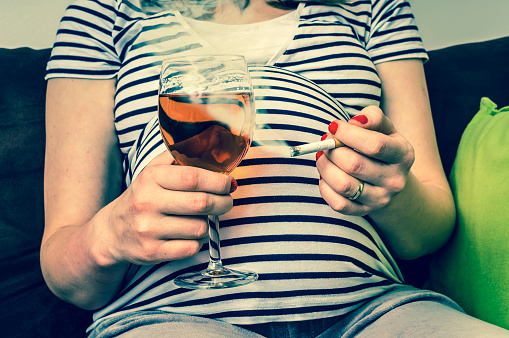 Těhotná žena v proužkovém tričku se cigaretou a sklenkou vína
