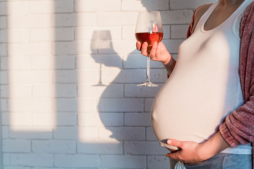 Těhotná žena se sklenkou vína v ruce