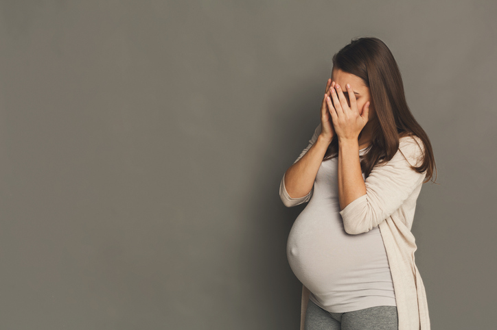Unavená tehotná žena, zakrývající si tvár rukama.