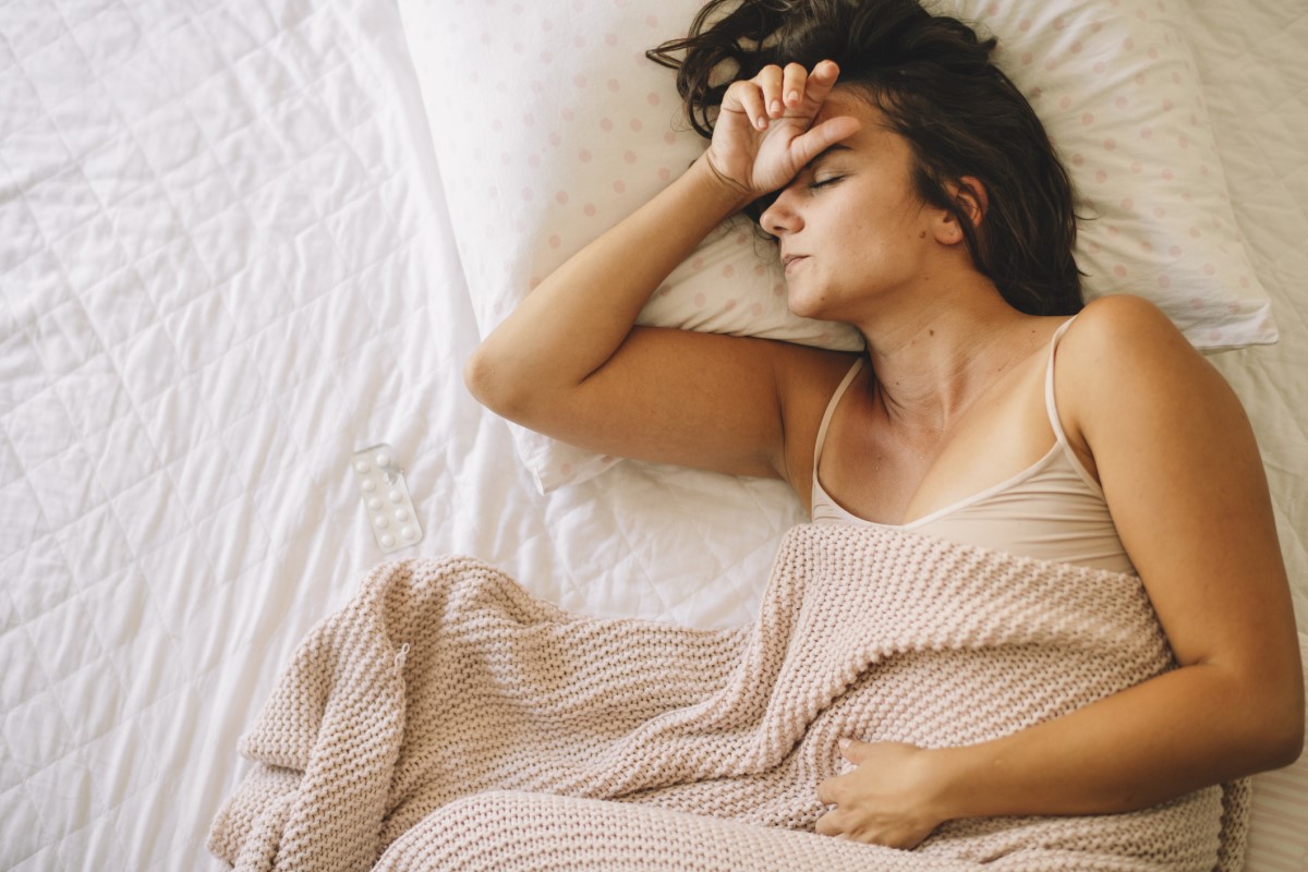 Unavená žena leží v posteli, bolí ji břicho