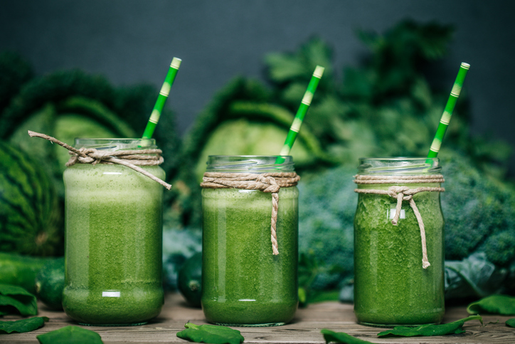 Zelené zeleninové smoothie, tři sklenice, v pozadí zelí, brokolice a hrách