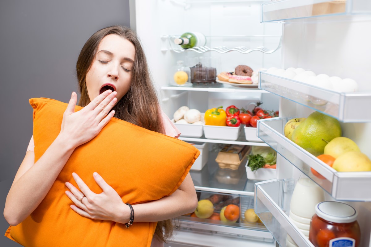 Žena spící vedle lednice, která ilustruje stravovací návyky jako faktor ovlivňující kvalitu spánku.