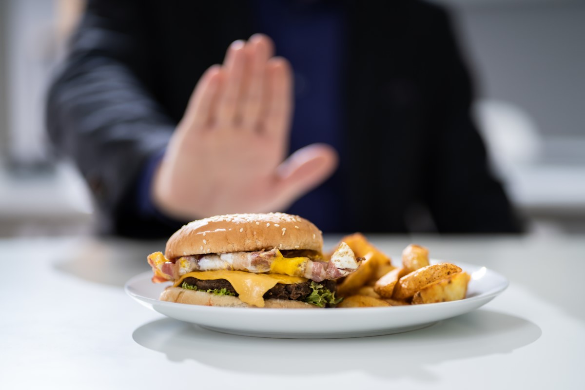 Nevhodné jídlo jako příčina pálení žáhy - hamburger na talíři, který muž odmítá