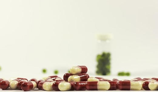 Léky volně rozsypané, červenobílé barvy a v pozadí léky zelené barvy v lahvičce