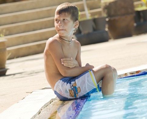 Chlapec sedí u bazénu, nohy ve vodě. je mu zima