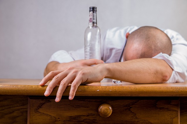 Alkoholismus je příčinou poruch nálady, muž leží na stole v ruce má prázdnou láhev alkoholu, alkoholik