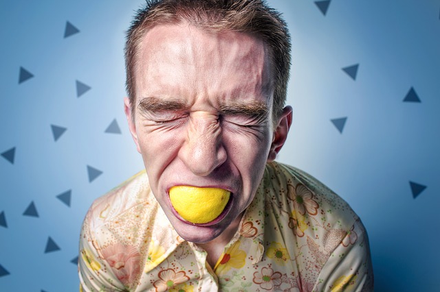 muž s citronem v ústech má kyselý výraz obličeje, možná alergická reakce na citrus