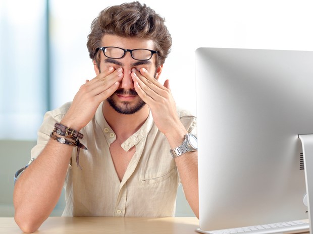Muž si drží bolestivé oči, má syndrom suchého oka pro dlouhodobou práci za počítačem