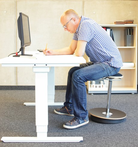Muž sedí za počítačovým stolem, má sedavé zaměstnání