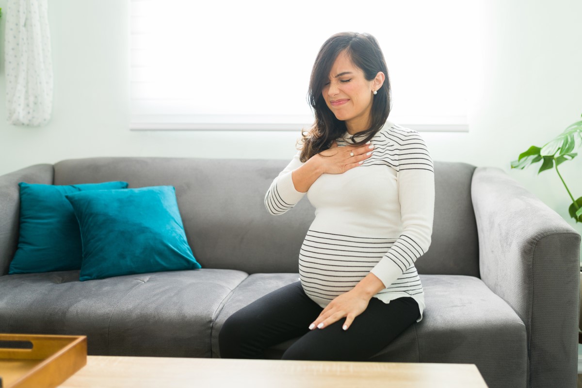 Pálení žáhy je časté u těhotných žen – těhotná žena sedí na sedačce a drží se za hruď
