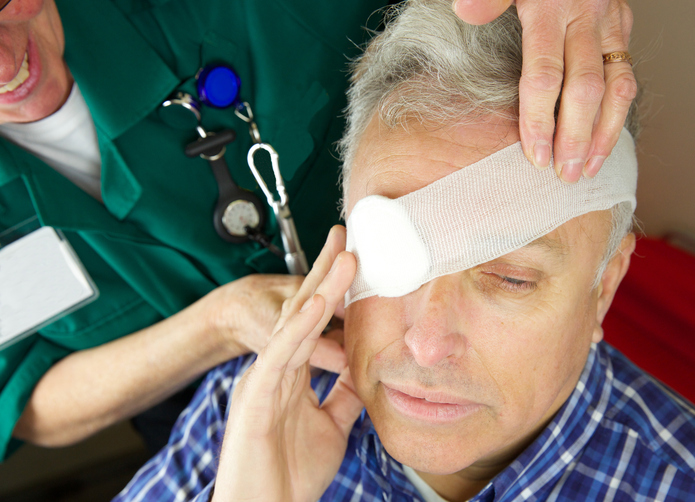 šedivý muž má ovázané oko, například po úraze, ošetřuje mu ho zdravotník